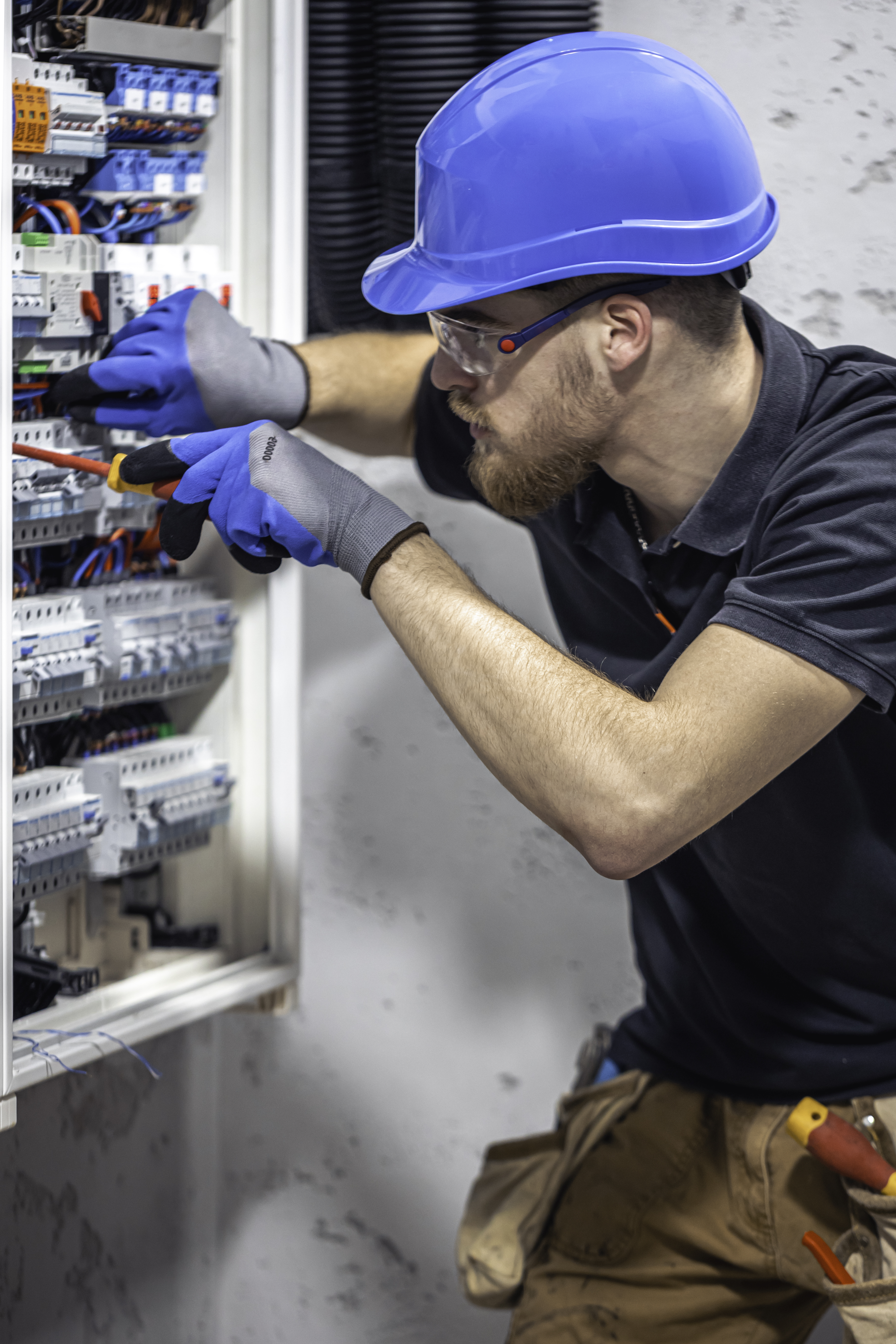 A male electrician works in a switchboard with an electrical connecting cable. Electrician with screwdriver tightens electrically operated switching equipment in fuse box.